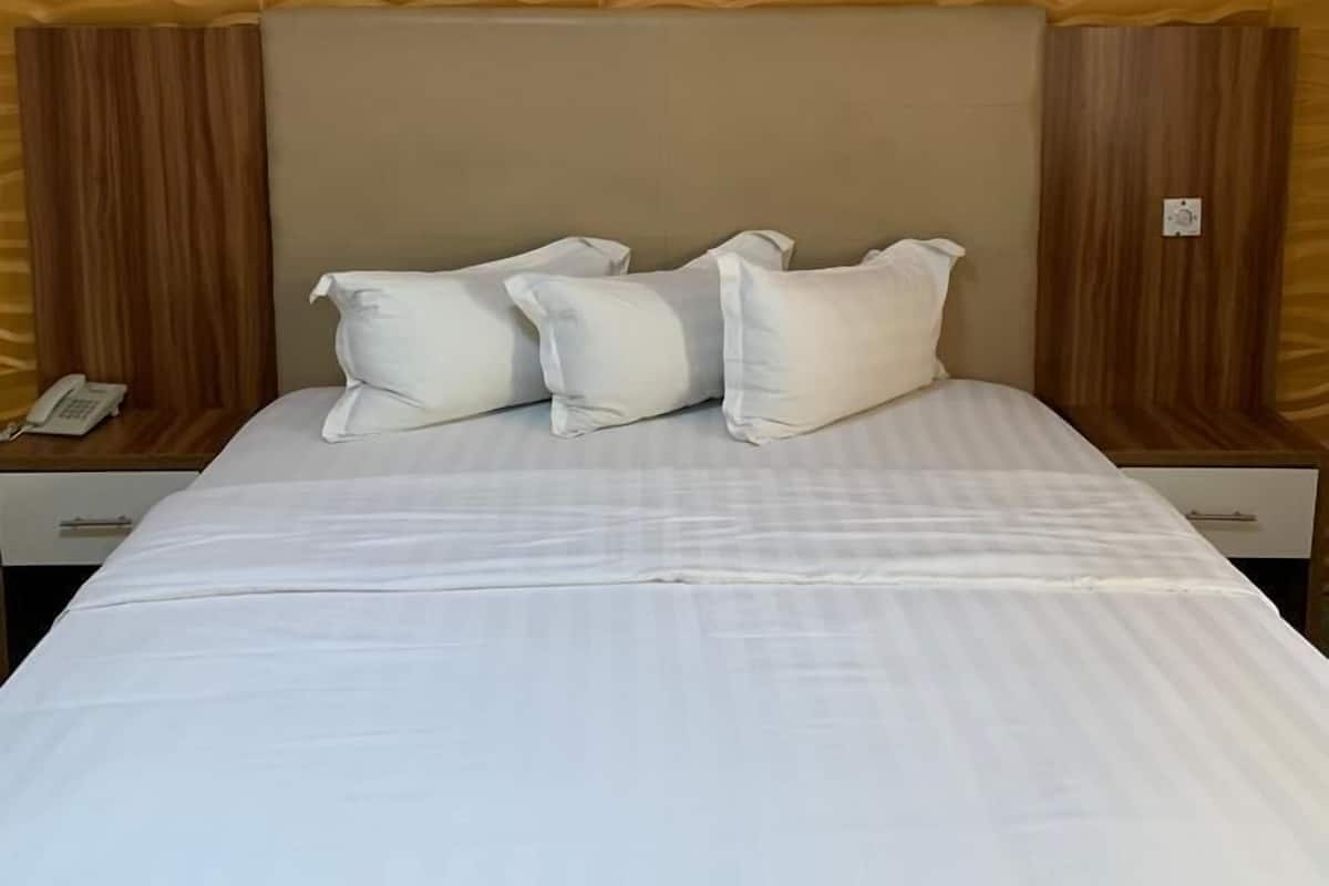 Une chambre d’hôtel avec un grand lit, une tête de lit au motif texturé et une table de chevet avec une lampe.