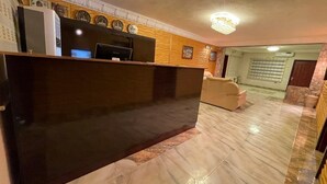 Un espace d’accueil doté d’un comptoir de réception en bois foncé, d’un téléviseur à écran plat et d’un canapé beige.