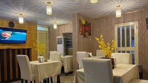 Un coin repas avec des tables disposées pour accueillir quatre personnes, un téléviseur fixé au mur et des fleurs jaunes décoratives sur les tables.