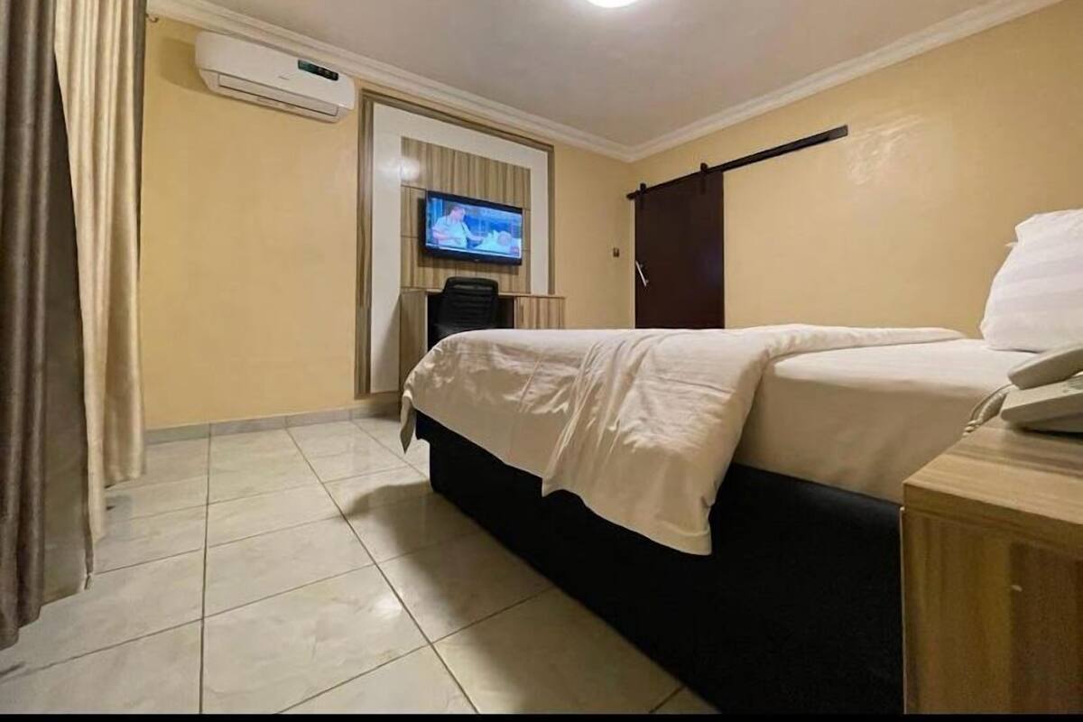 Une chambre d’hôtel équipée d’un lit, d’une télévision, d’un climatiseur et d’une armoire en bois.