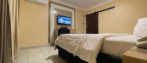 Una habitación de hotel con una cama, un televisor, aire acondicionado y un armario de madera.