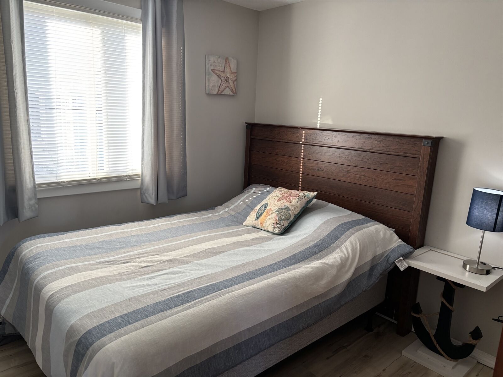 Un dormitorio con cama, mesita de noche, lámpara, decoración con estrellas en la pared y ventana con cortinas.