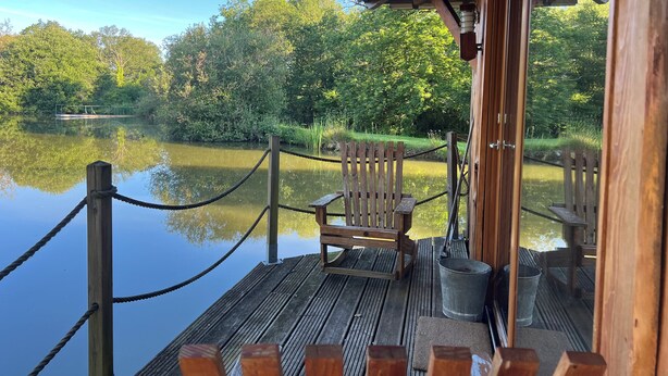A wooden deck with a view of a calm lake, surrounded by lush greenery. - Domaine de la Vergnolle (Roches)