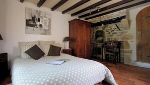 A bedroom with a bed, a wooden cabinet, a stone wall, and a fireplace. - Domaine de la Vergnolle (Roches)