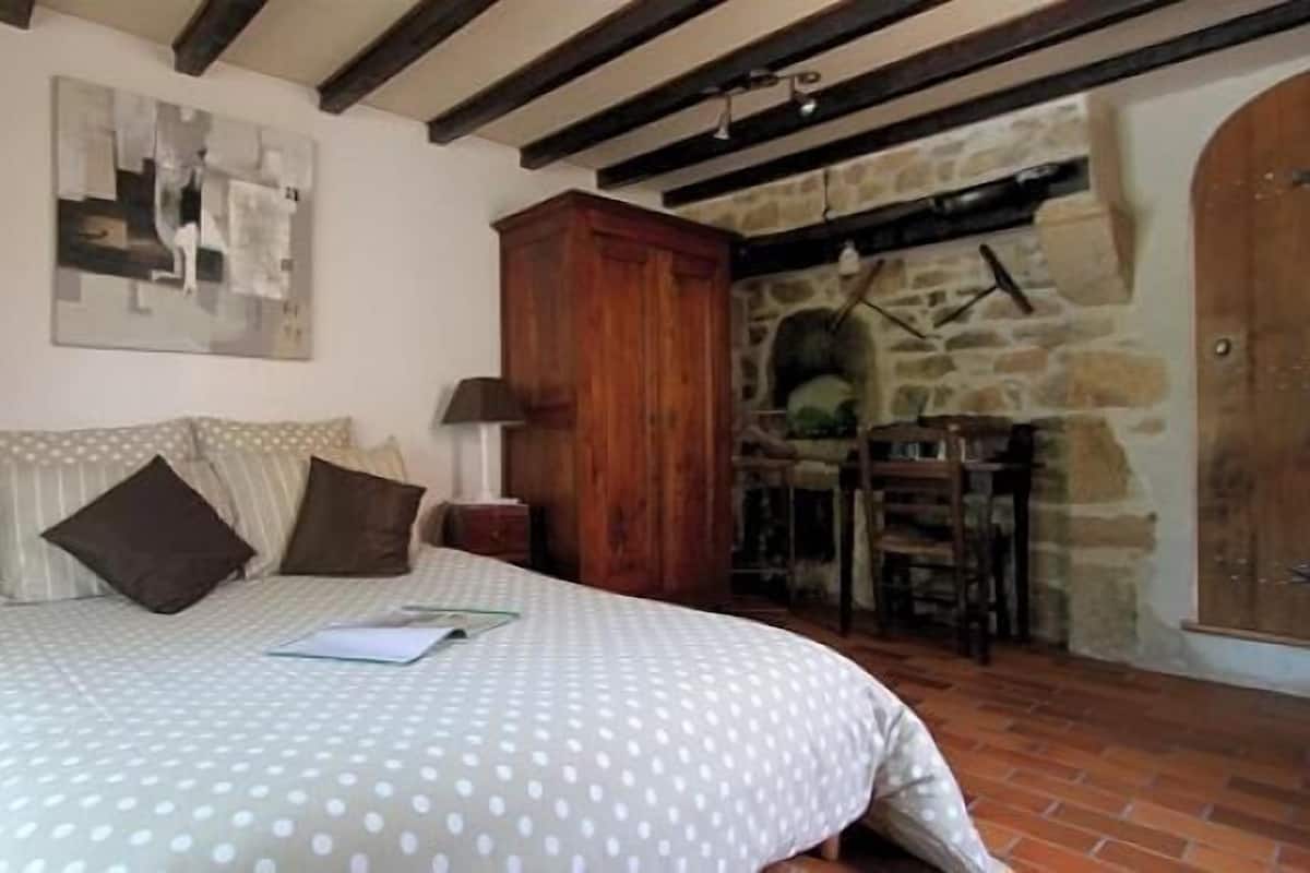 Une chambre à coucher avec un lit, une armoire en bois, un mur en pierre et une cheminée.