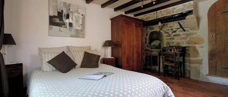 A bedroom with a bed, a wooden cabinet, a stone wall, and a fireplace.
