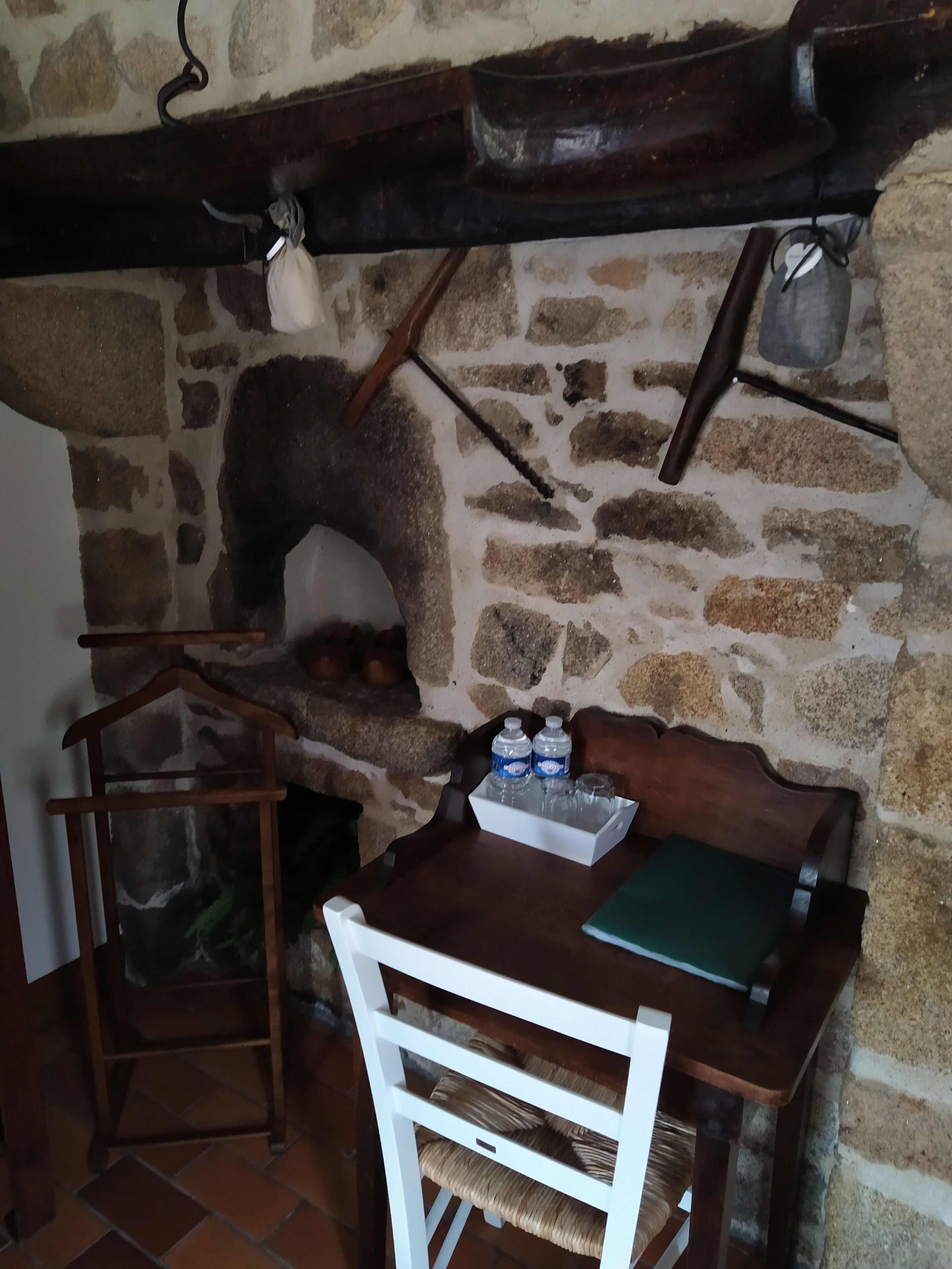 A rustic stone wall with a wooden bench and table, a hanging light fixture, and a small shelf with bottles and glasses.