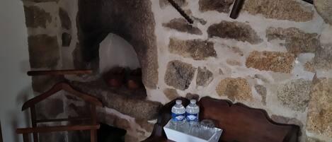 A rustic stone wall with a wooden bench and table, a hanging light fixture, and a small shelf with bottles and glasses.