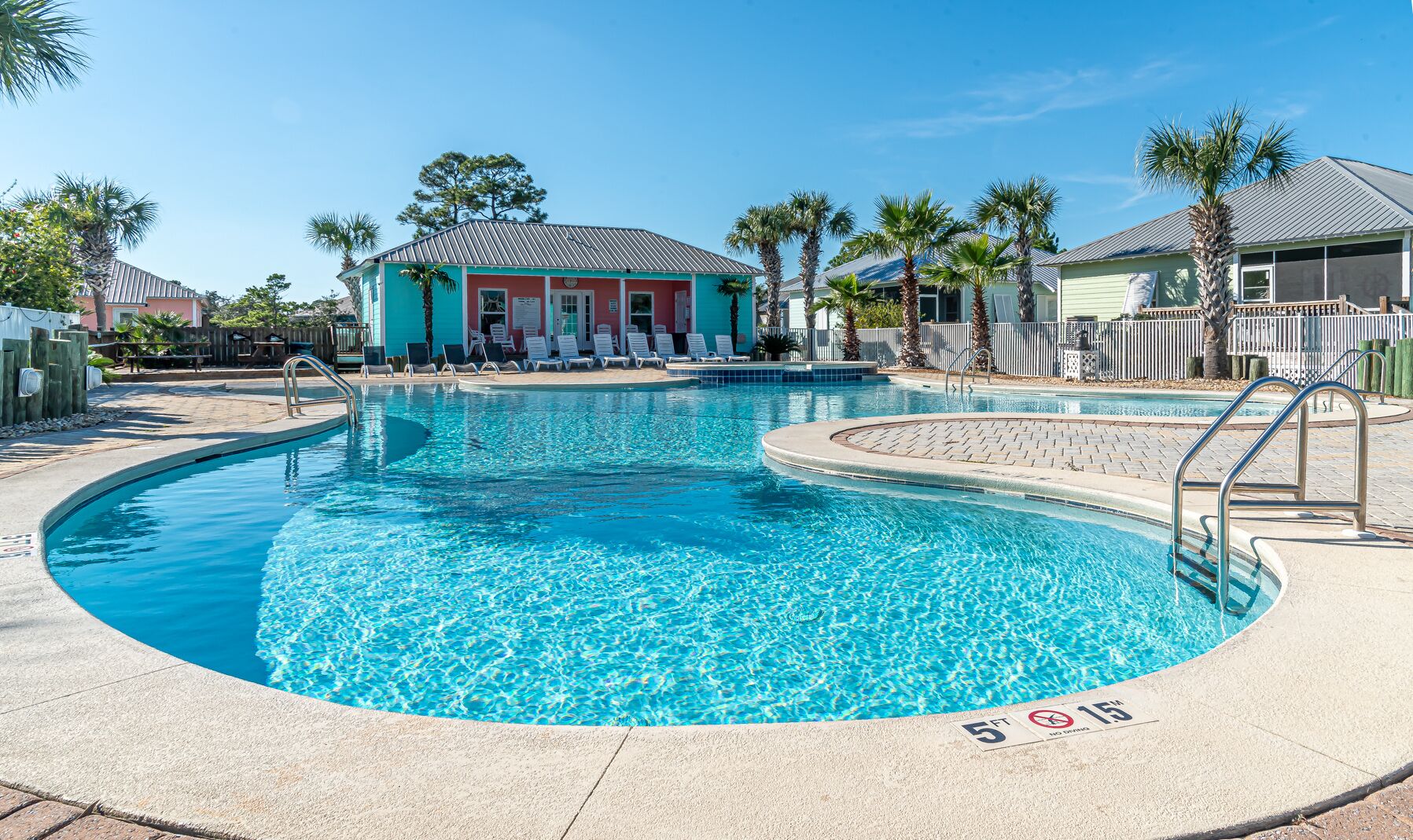 A swimming pool with a 5 ft depth limit, surrounded by lounge chairs and palm trees.