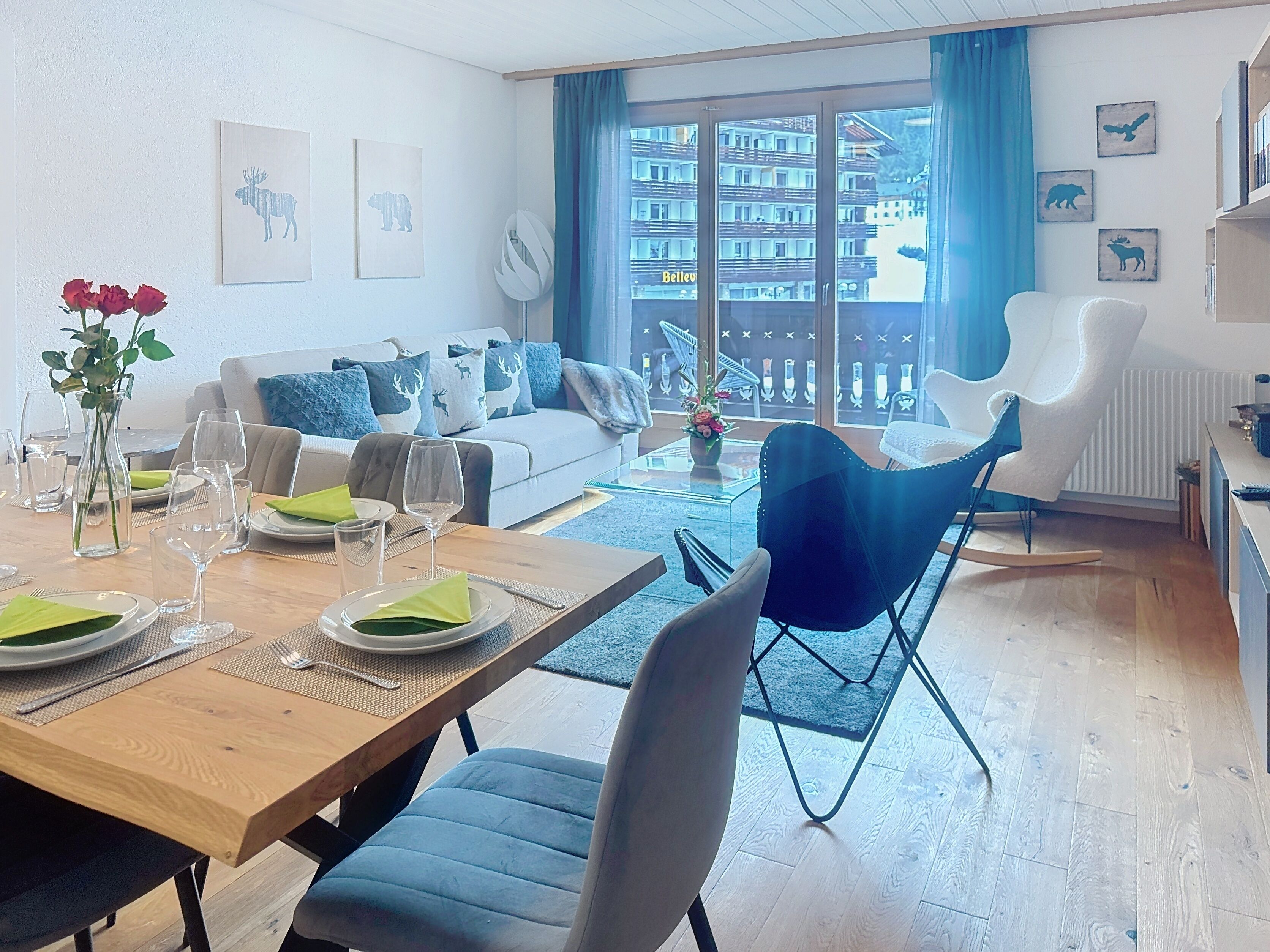 A modern living room with a dining area, featuring a wooden table set for four, a blue sofa, and a blue chair.