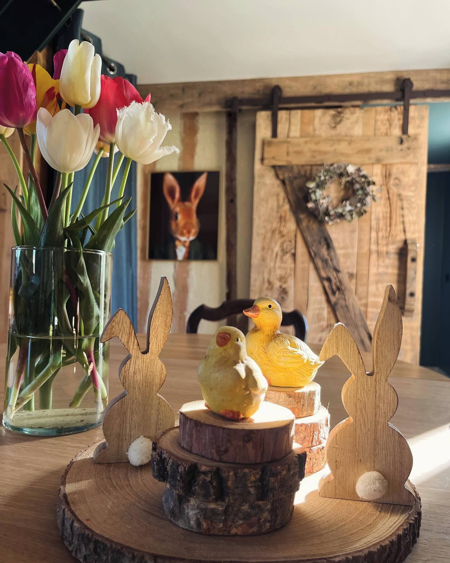 Ein Holztisch mit einer Tulpenvase, Holz-Hasenfiguren und einer Holz-Entenfigur.