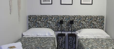Una camera da letto con due letti, ciascuno con copripiumini a motivi floreali, cuscini bianchi e una testiera con decorazioni a foglia. Sulla parete sopra i letti sono appese tre immagini incorniciate.