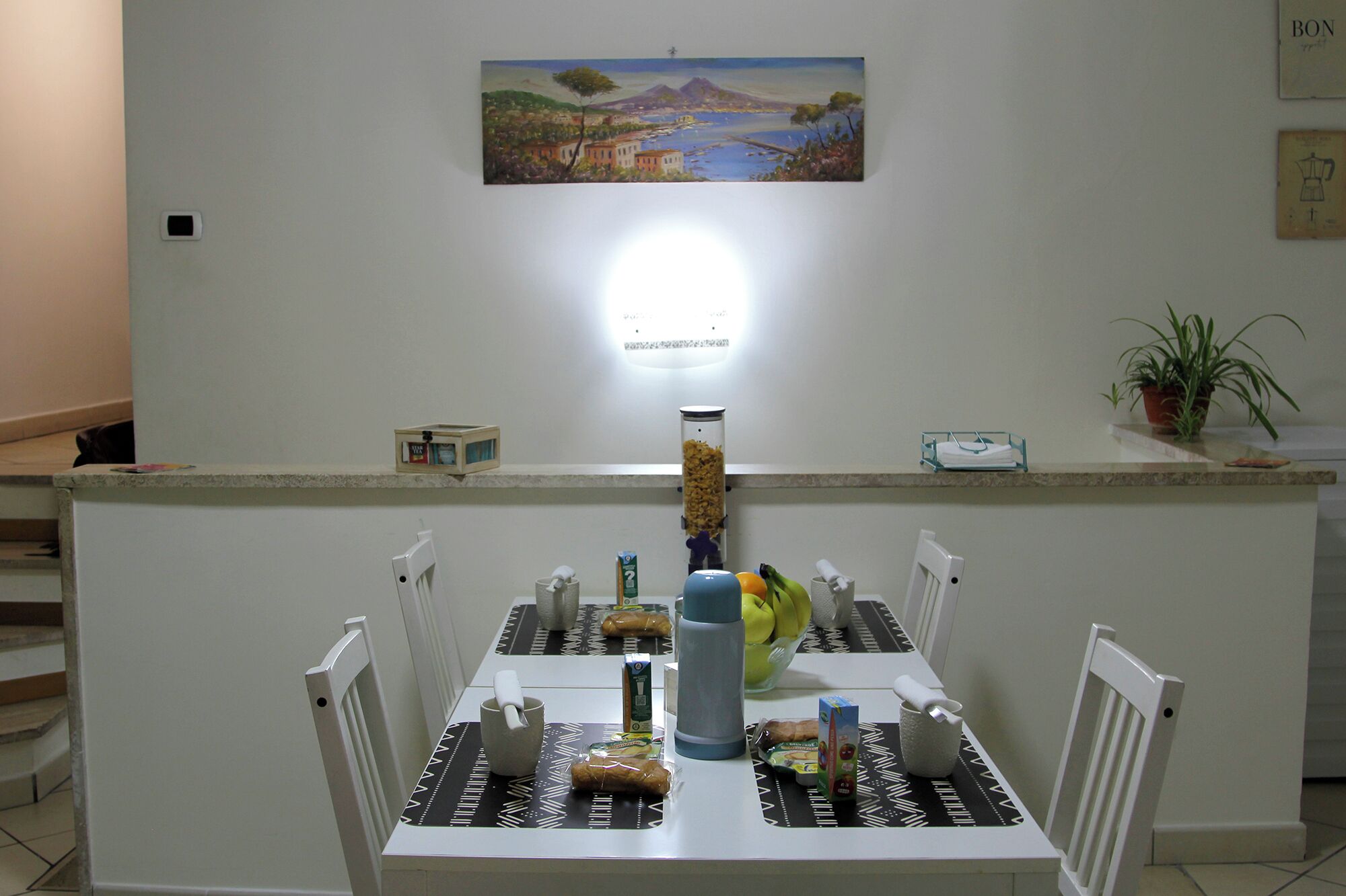 Een eethoek met een tafel gedekt voor twee personen, een koffieapparaat en een schilderij aan de muur.