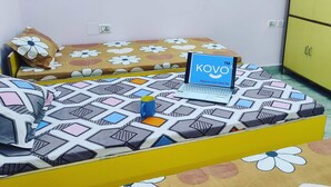 A room with a bed featuring a geometric patterned bedspread, a laptop on the bed, and a yellow wardrobe. - Kovo Expo Mart (Greater Noida)