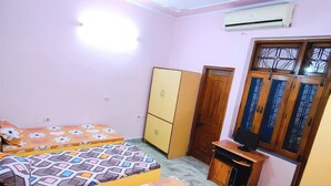 A bedroom with two beds, a wardrobe, a desk with a computer, and a window with decorative iron bars. - Kovo Expo Mart (Greater Noida)