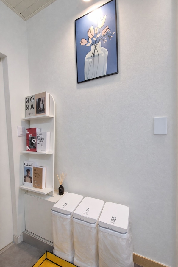 Un baño limpio y moderno con una pared blanca, una obra de arte enmarcada sobre un estante blanco, y tres cubos de basura debajo.