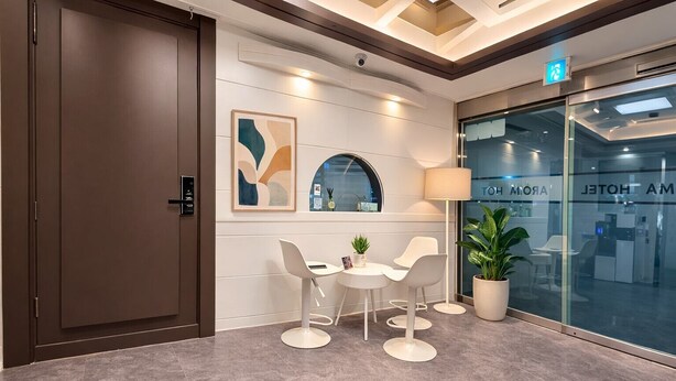 A modern hotel lobby with a reception desk, seating area, and a large window with a view of the interior. - Aroma Hotel (Seoul)