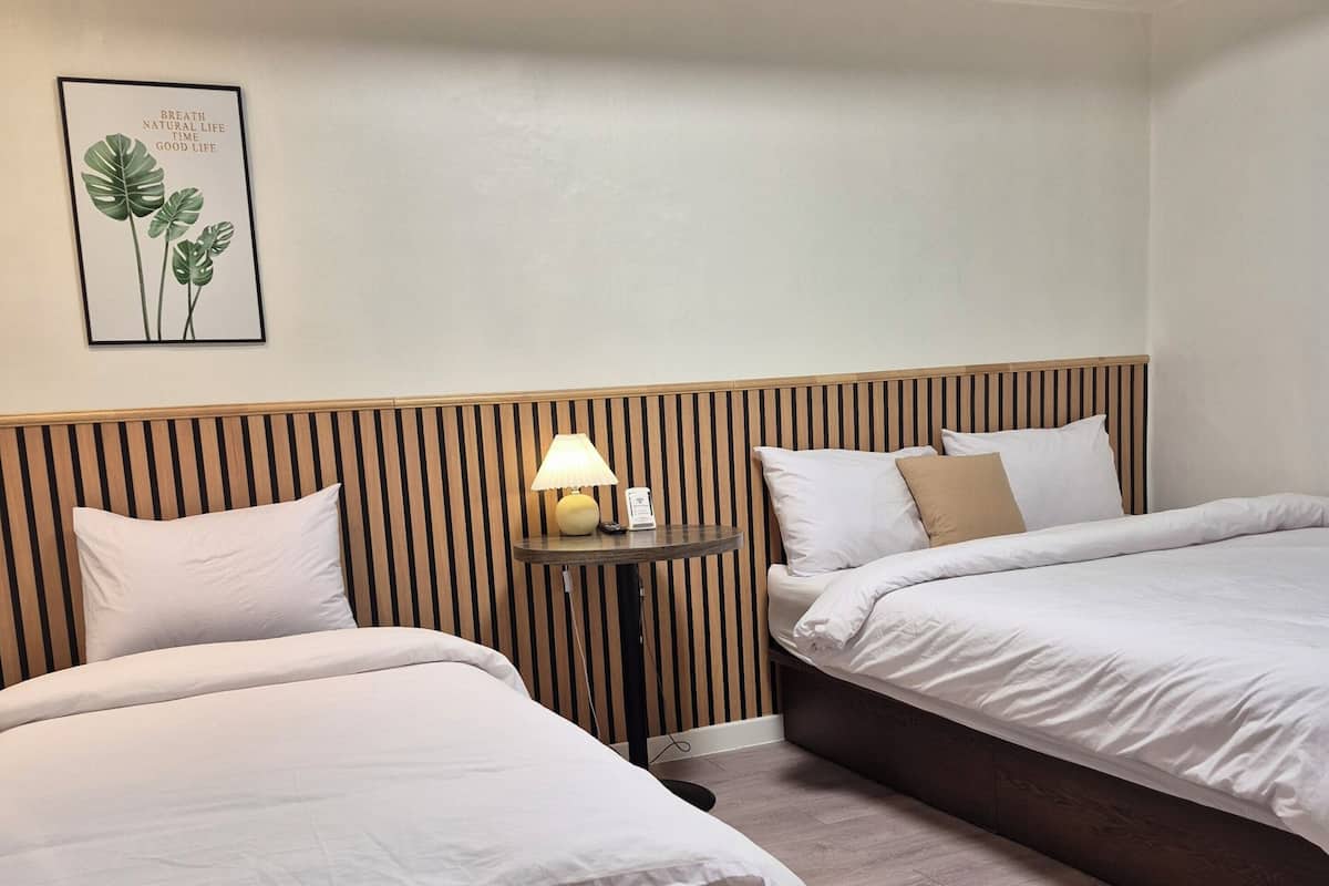 A hotel room with two beds, a bedside table with a lamp, a framed quote on the wall, and wooden paneling on the headboard.