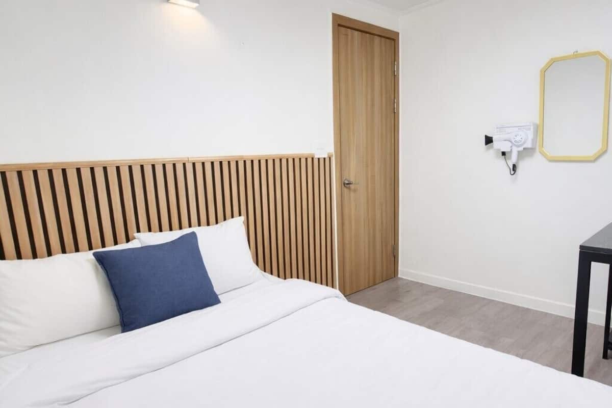 A modern bedroom with a bed, a wooden slatted headboard, a door, a wall-mounted mirror, and a ceiling light.
