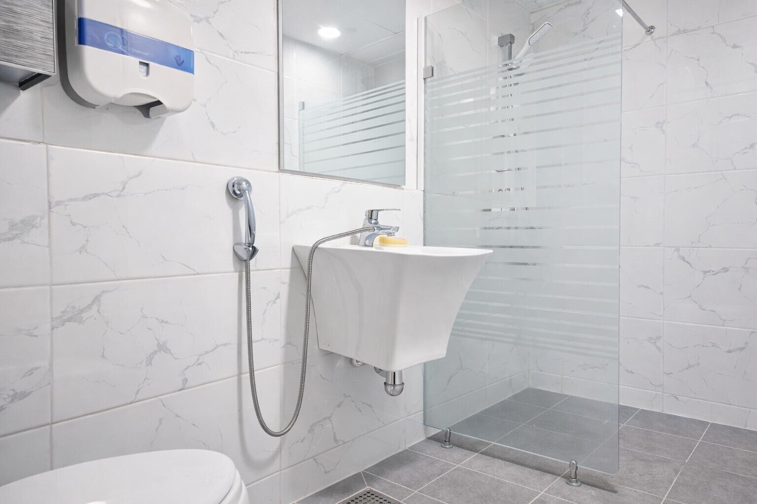 A modern bathroom with a toilet, a sink, a shower with a glass door, and a hand dryer.