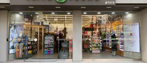 The exterior of a store named 'OLIVE YOUNG' with a glass entrance and various products displayed inside.