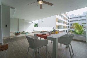 A modern outdoor dining area with a table and chairs, a ceiling fan, and a view of the building's exterior. - Fantastic Beach Condo w/ private Picuzzi (Punta Cana)