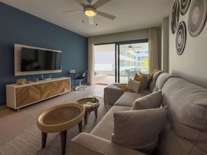 Een woonkamer met een bank, televisie, houten kast en een eethoek met tafel en stoelen.