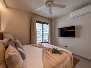 A hotel room with a bed, a ceiling fan, a TV, and a window with curtains. - Fantastic Beach Condo w/ private Picuzzi (Punta Cana)