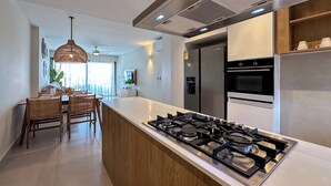 A modern kitchen with a central island, stainless steel appliances, and a dining area with wicker chairs. - Gorgeous new beach condo w/ PIcuzzi (Punta Cana)