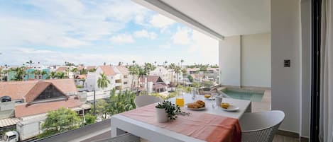 A balcony with a table set for breakfast, overlooking a residential area with houses and palm trees.