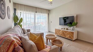 A modern living room with a sofa, ottoman, coffee table, and TV stand. - Gorgeous new beach condo w/ PIcuzzi (Punta Cana)