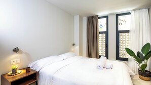 Une chambre d’hôtel avec un lit, une table de chevet avec une lampe, une plante en pot et une fenêtre avec des rideaux.