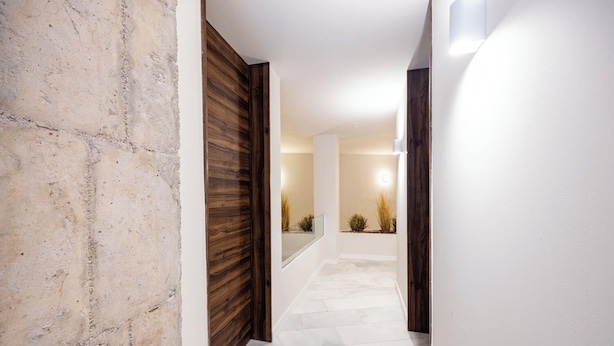 Un couloir avec un mur en pierre, une porte en bois et un sol carrelé de carreaux blancs.