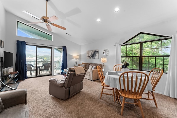 A spacious living area with a ceiling fan, a large window with a view, a dining table with chairs, and a sofa. - Penthouse Quiet End Unit • Near Strip + Pool (Branson)