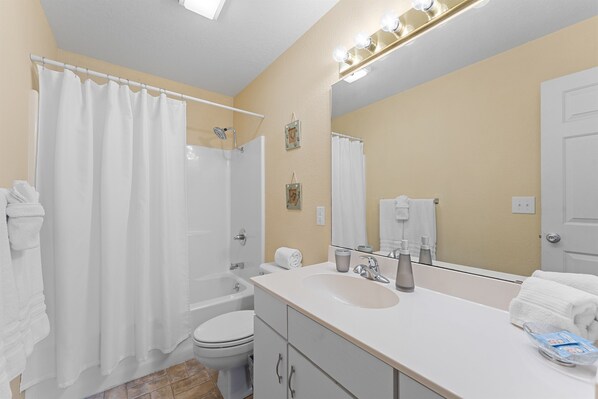 A bathroom with a shower curtain, a sink, a toilet, and a mirror. - Penthouse Quiet End Unit • Near Strip + Pool (Branson)