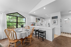 A modern kitchen with white cabinets, a central island, and a dining area with wooden chairs and a table. - Penthouse Quiet End Unit • Near Strip + Pool (Branson)