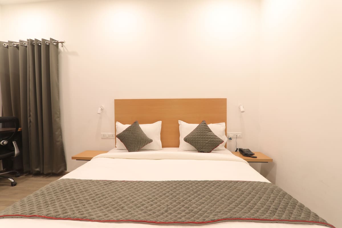 A hotel room with a bed, two pillows, a bedside table with a phone, and a chair.