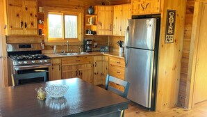 A cabin-style kitchen with wooden cabinets, a stainless steel refrigerator, a stove, and a dining table with chairs. - Charming secluded 2-bedroom cabin with WiFi, AC in peaceful Richland Center (Richland Center)