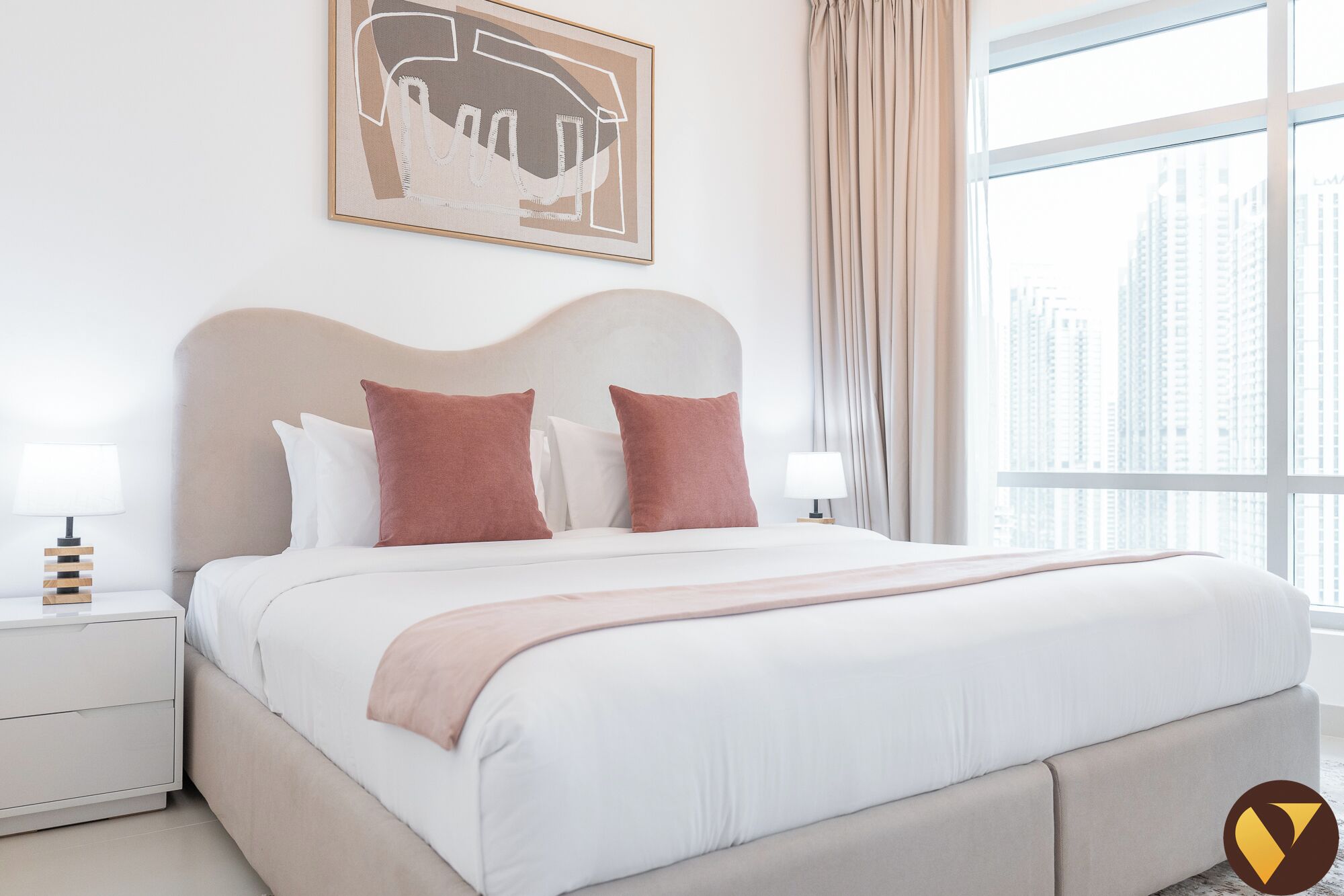 A hotel room with a large bed, two bedside tables, a city view, and a framed artwork on the wall.