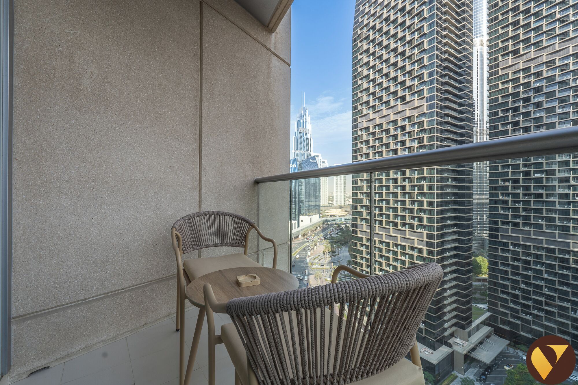 Een balkon met uitzicht op hoge gebouwen, een tafel en twee rieten stoelen.