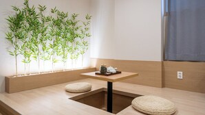 A minimalist room with a low table, two cushions, a small plant wall, and a window with a view. - GOYU HOTEL (Suwon)