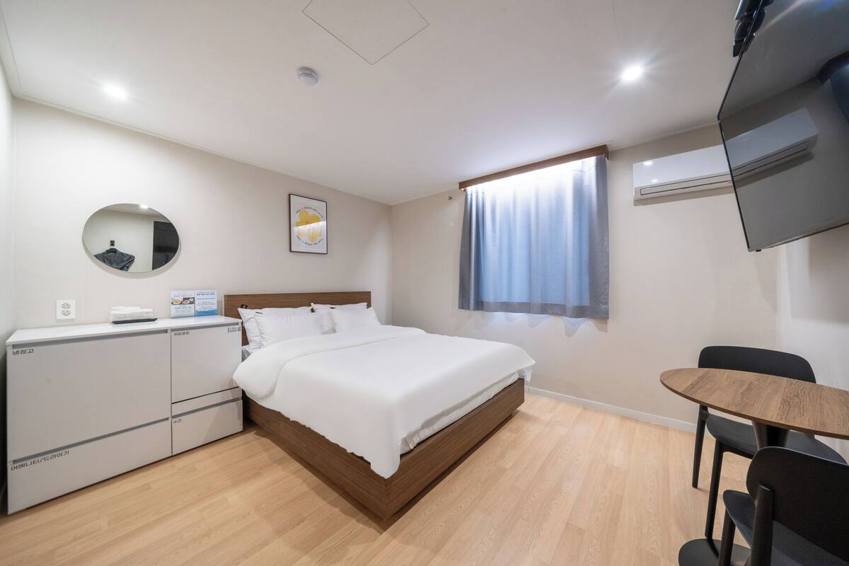 Une chambre d’hôtel équipée d’un lit, d’un bureau, d’une chaise, d’une télévision, d’un miroir et d’une fenêtre avec des rideaux.