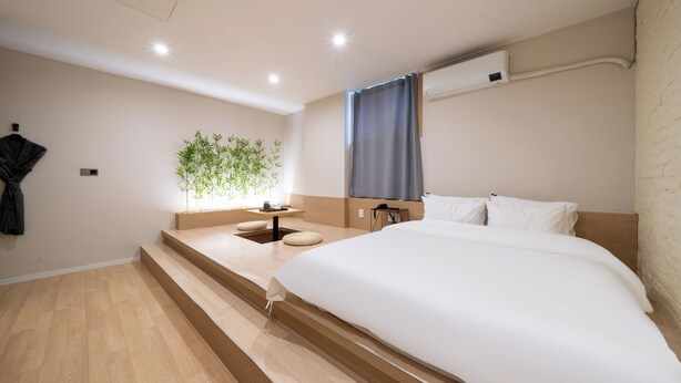A modern hotel room with a large bed, a small desk, a plant, and a window with curtains. - GOYU HOTEL (Suwon)