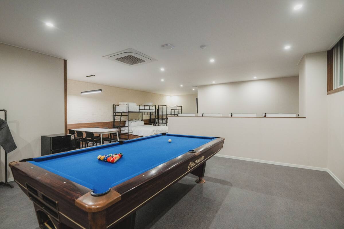 Une table de billard dans une pièce équipée de lits superposés et d’une table de ping-pong.