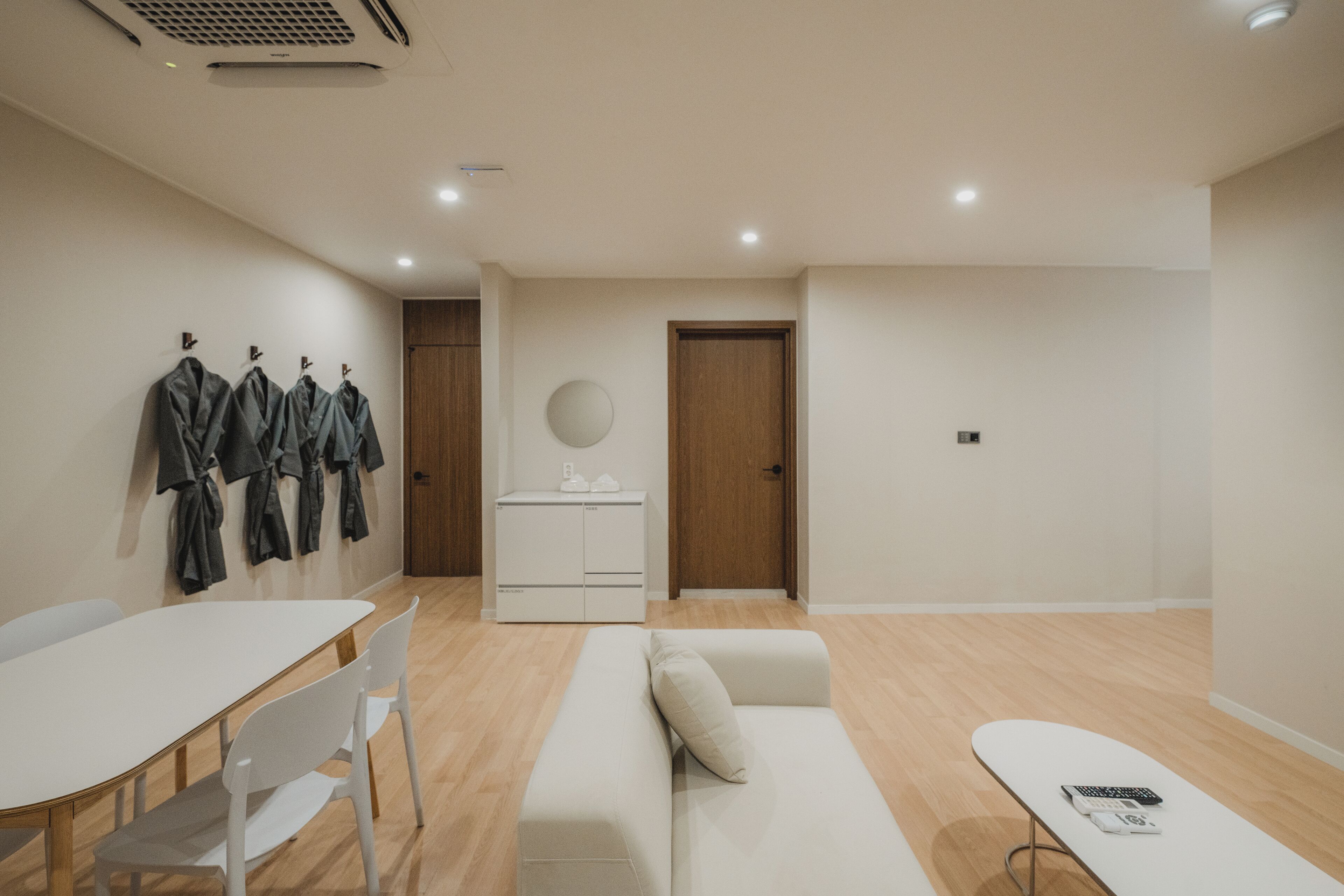 A modern, minimalist room with a white table, chairs, a sofa, and a small kitchenette.