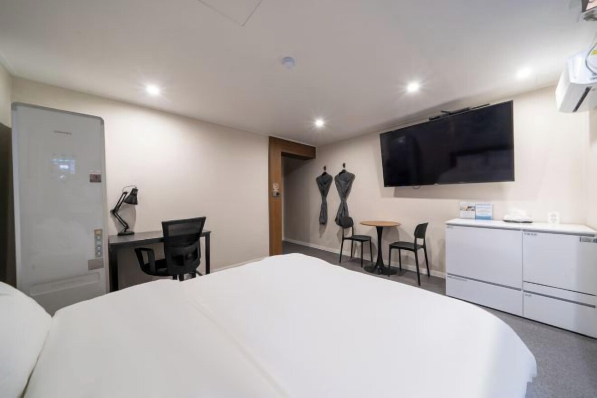 A hotel room with a bed, a desk with a chair, a small table with two chairs, a TV mounted on the wall, and a mini-fridge.