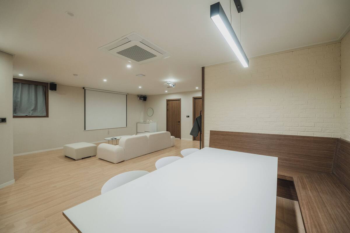 Une salle de réunion moderne, dotée d’une grande table blanche, d’un canapé et d’un écran de projection.
