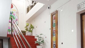 A staircase with red steps and a wooden handrail, leading to an upper floor. There are potted plants on the steps and a decorative wall hanging above.