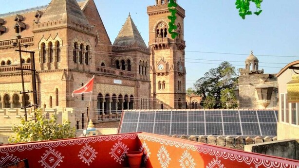A terrace with a bench, solar panels, and a view of a historic building with a clock tower.
