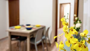 Ein Essbereich mit einem Tisch für zwei Personen, Stühlen und einem Strauß gelber Blumen im Vordergrund.